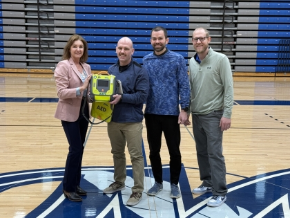 Left to right, Jessica Bortner hands off an AED to the Sports Medicine Team, represented by Community Hospital Athletic Trainer Evan Dekok and Physical Therapists Brett Burton and Ryan Hardin.